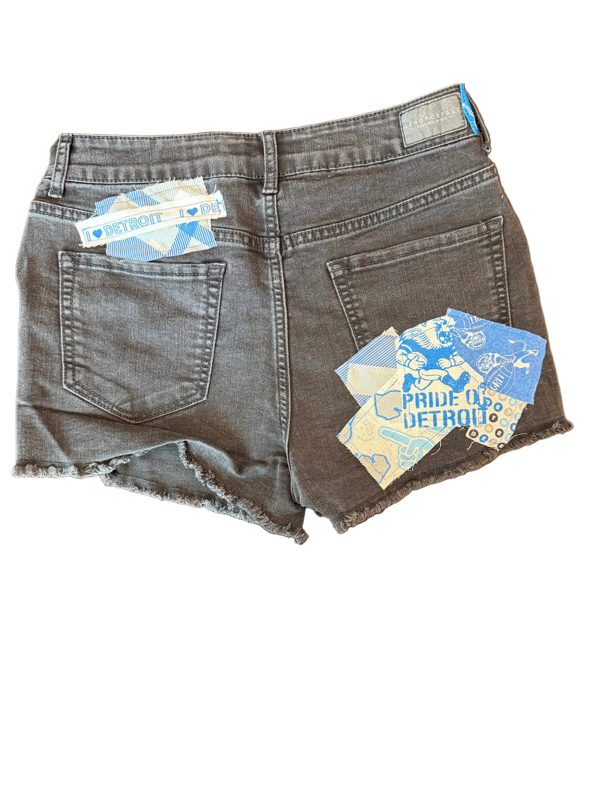 A pair of folded gray denim shorts with raw, frayed hems and visible blue-and-white brand tags, placed on a dark wooden tabletop.