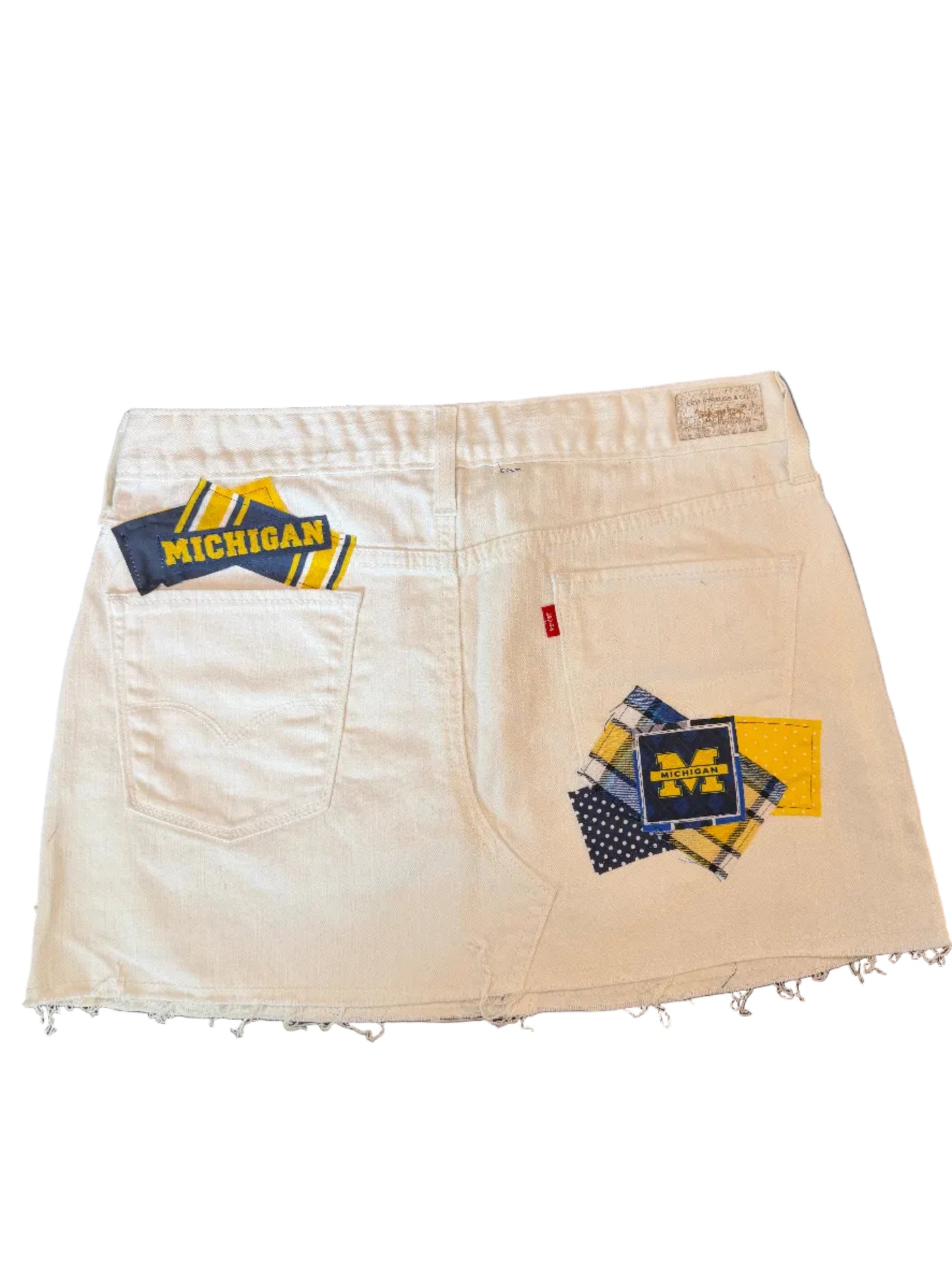 A pair of off-white denim shorts featuring distressed frayed hems and Michigan Wolverines themed patches on the back pockets.