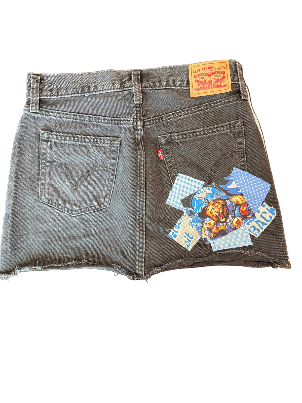A pair of dark gray Levi's denim shorts laid flat on a wooden table, featuring a colorful cartoon patch on the back pocket and the classic red tab.