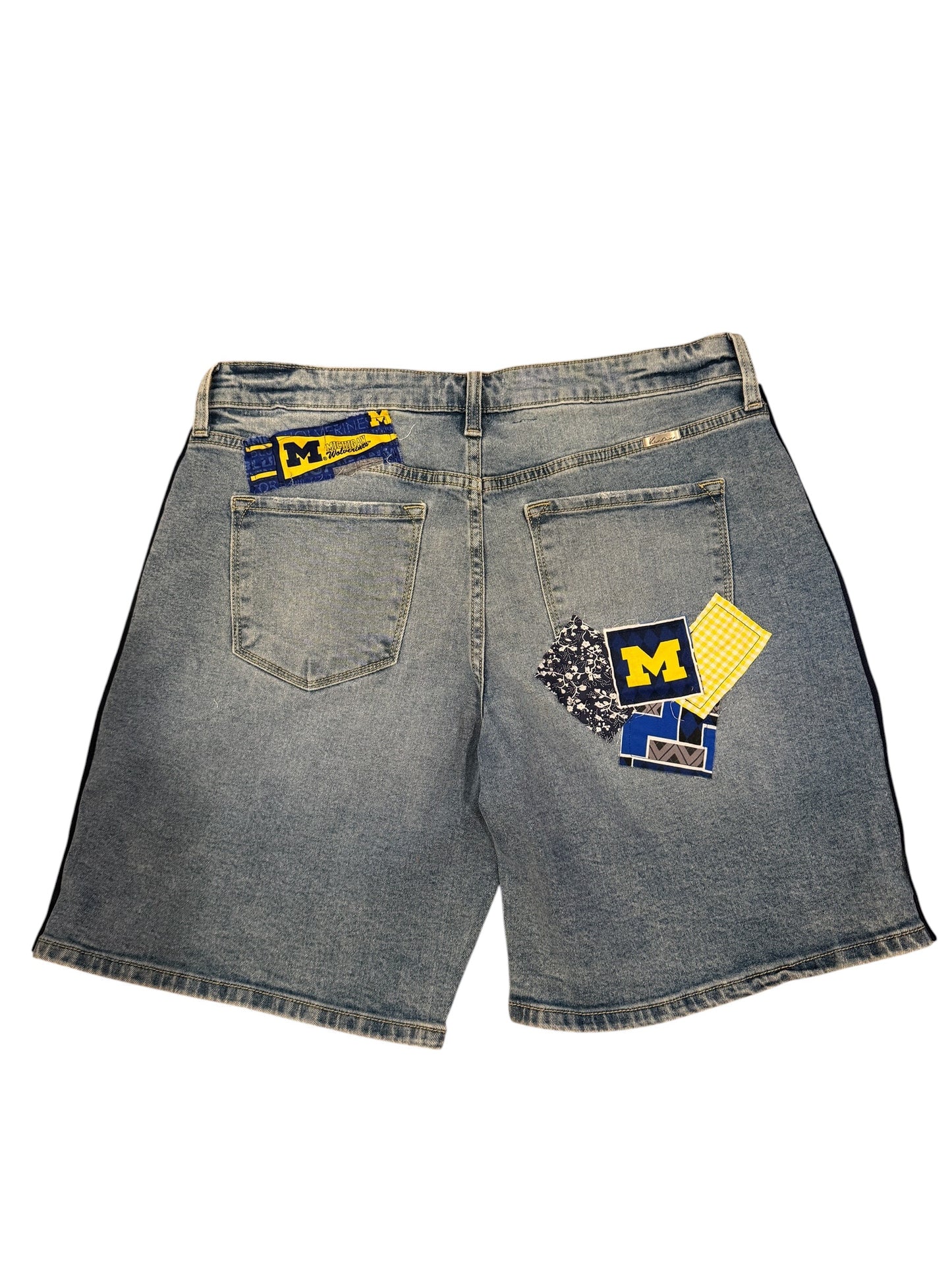 Light wash denim shorts shown from the back, featuring a blue and yellow Michigan Wolverines patch on the right back pocket and a smaller matching patch on the left back pocket.