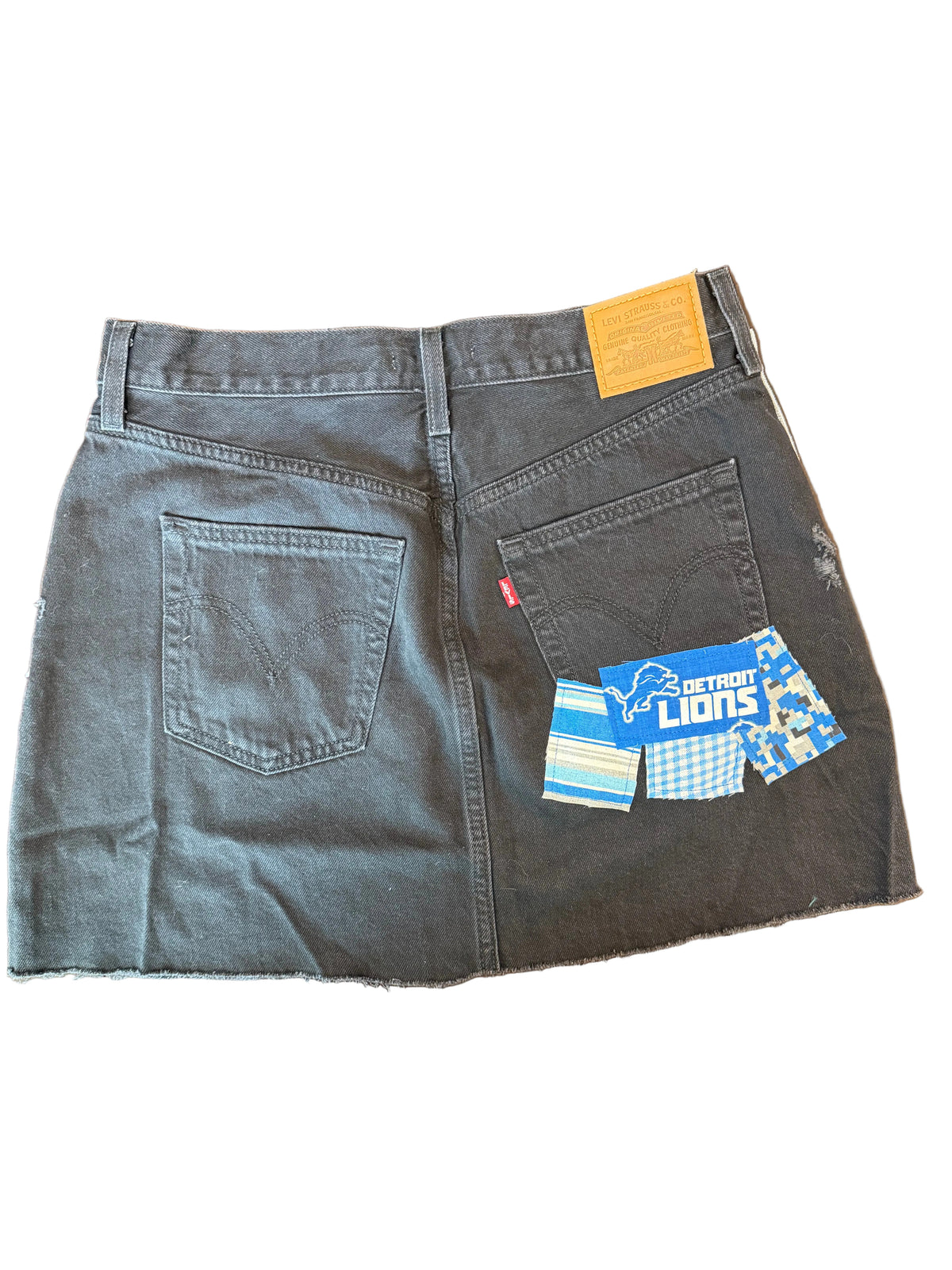 A pair of dark gray Levi's denim shorts with raw, frayed hems, laid flat on a wooden floor. The iconic blue and white Levi's fabric tag is visible on the back pocket, along with the signature red tab.