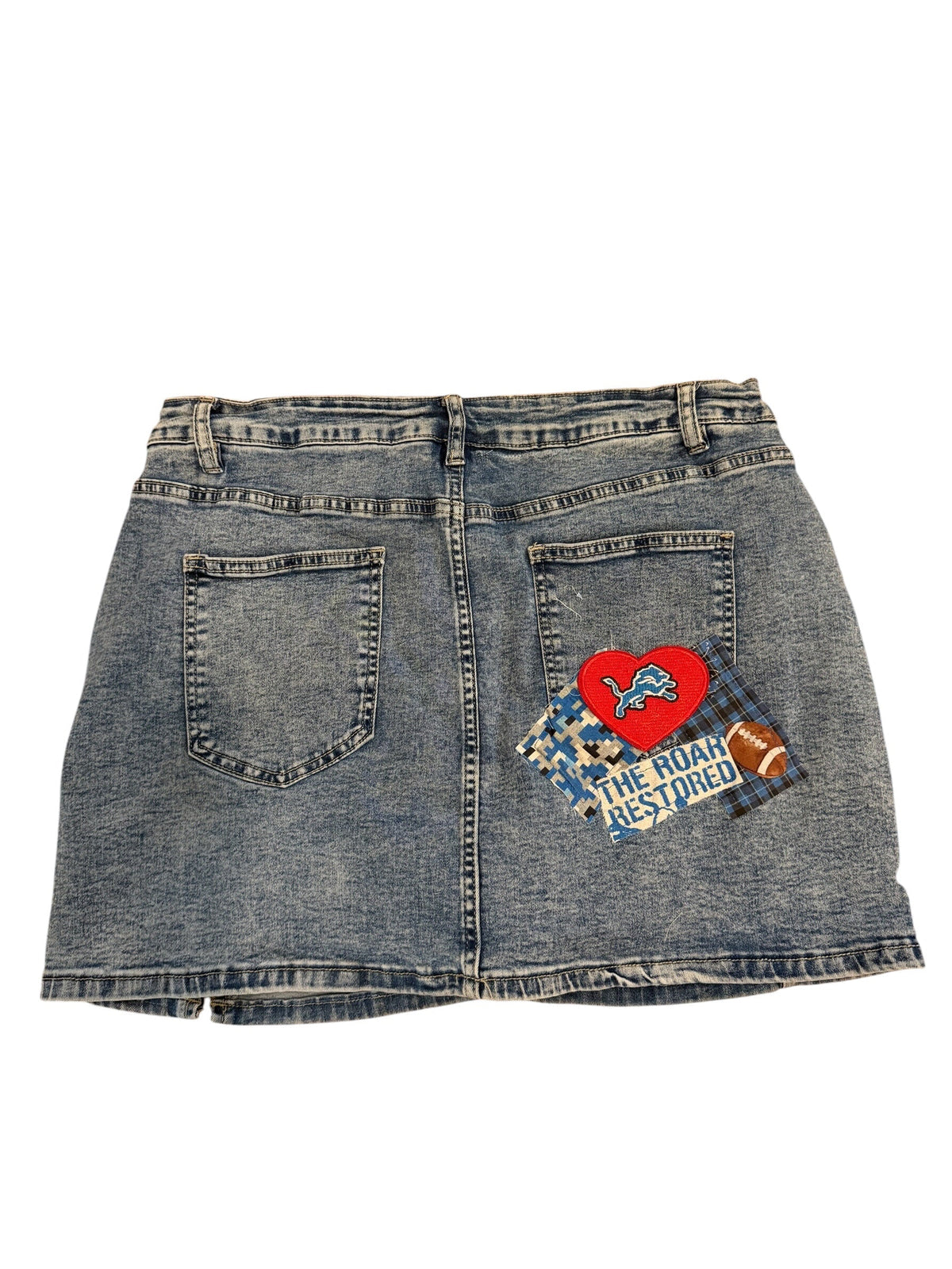 A pair of faded blue denim shorts shown from the back, featuring a red heart patch and a blue patterned patch with the text 'THE ROCK IS YOUNG' on the left side.