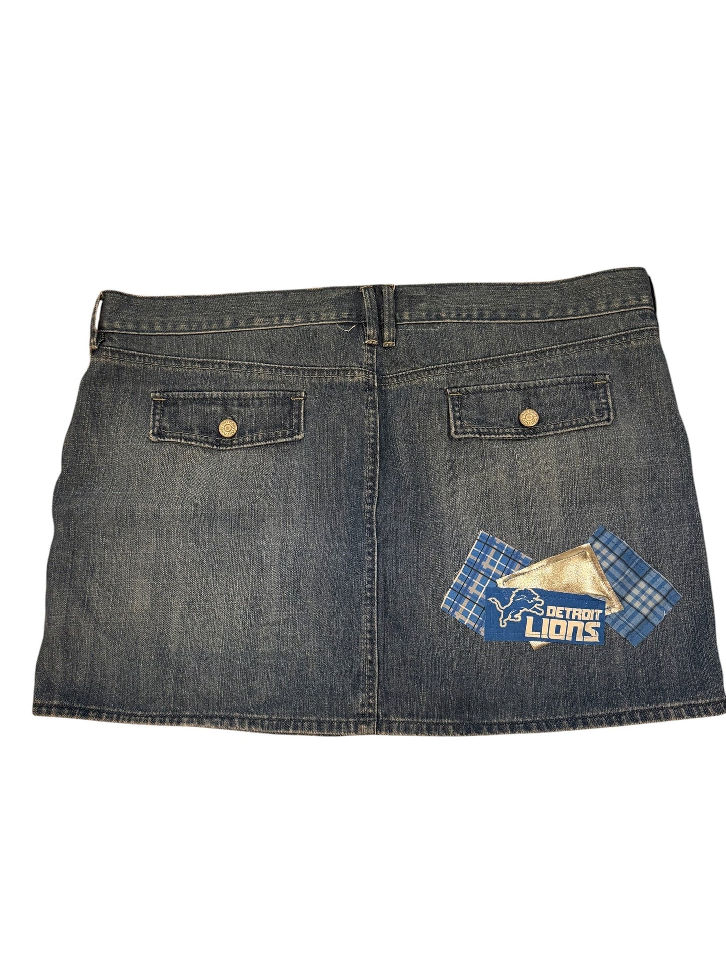 A dark gray denim skirt with two buttoned flap pockets and a blue plaid 'Lions' patch on the upper right side, shown flat against a white background.