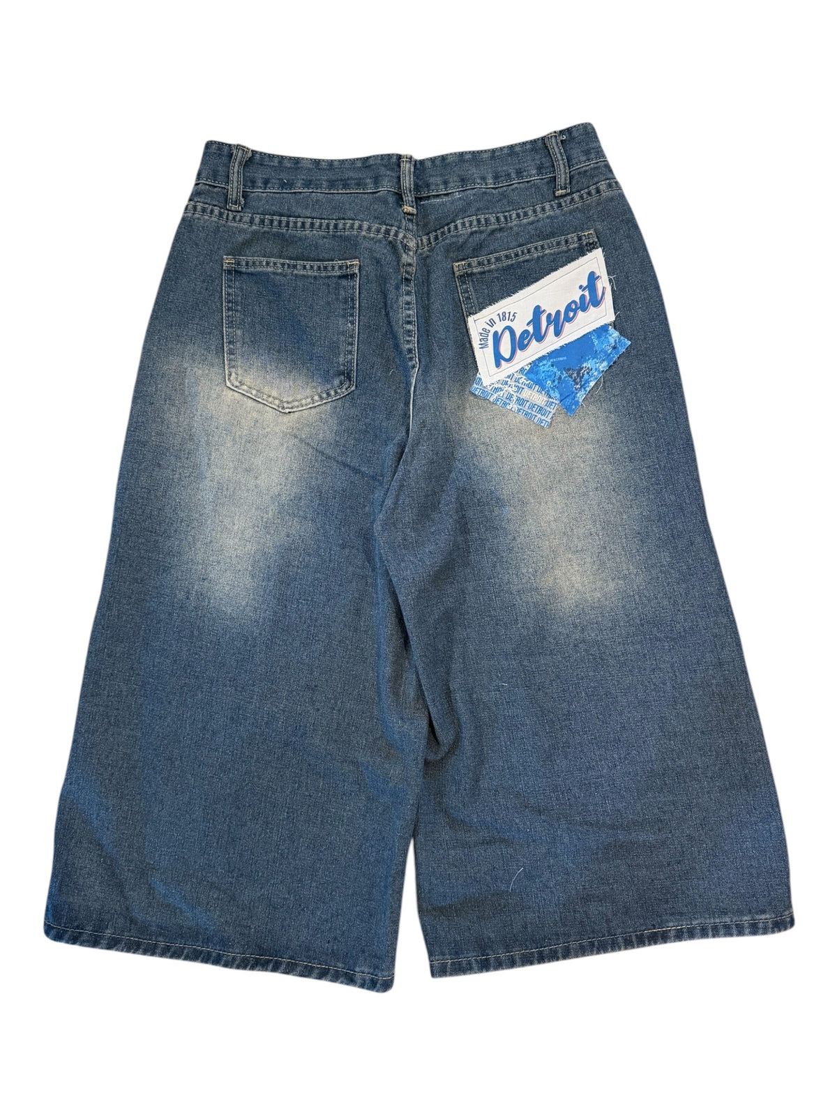 A pair of blue denim shorts with a faded white wash on the front, laid flat on a white background. A blue and white 'The Outfitter' brand tag is attached to the back pocket.