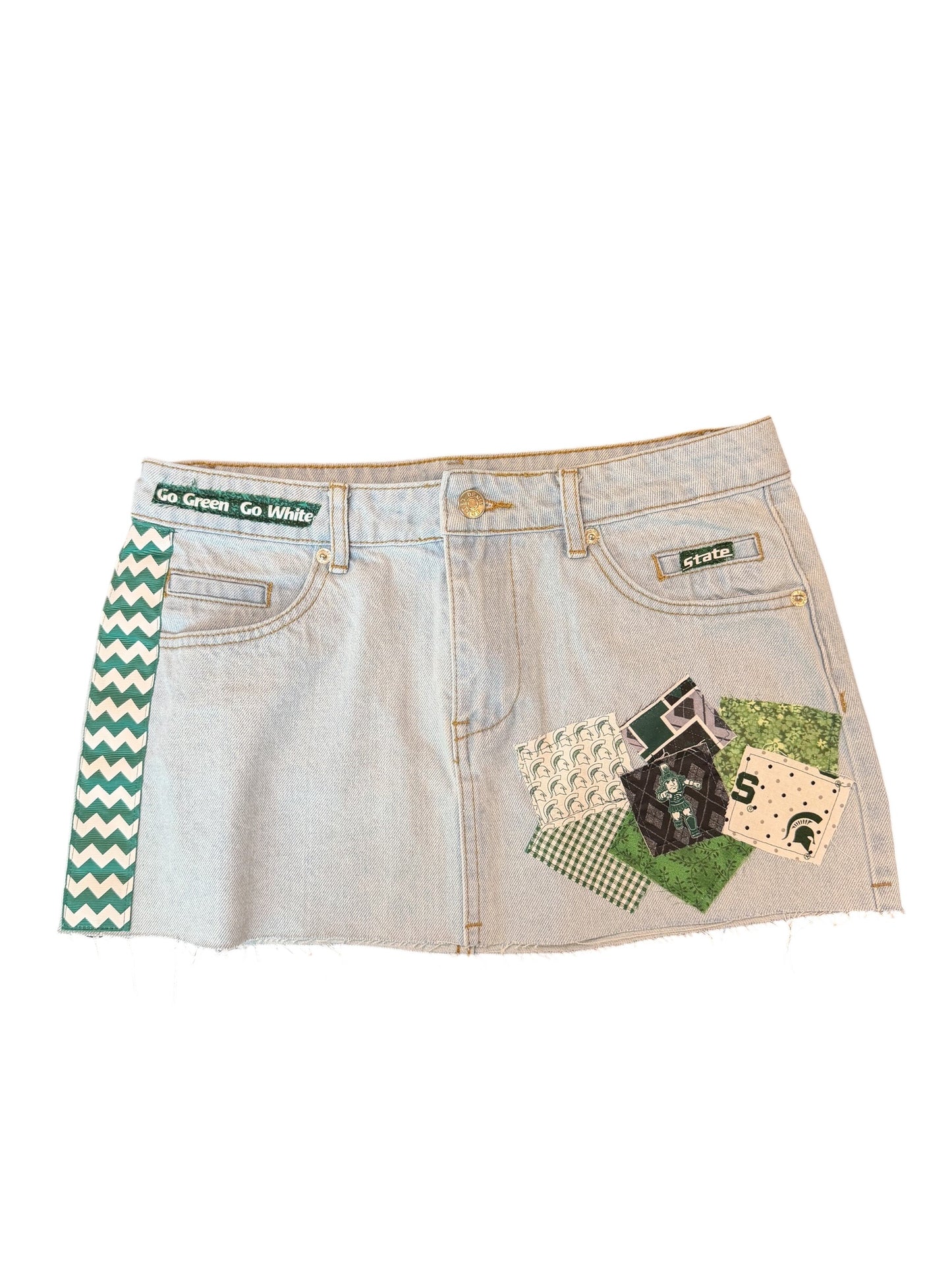 A light-wash denim mini skirt featuring a green and white chevron pattern on the left side seam and a green, black, and beige patchwork design on the right side pocket. The waistband displays a 'LSU Green: Go White' label, and a small 'RENEW' brand tag is visible on the right pocket.