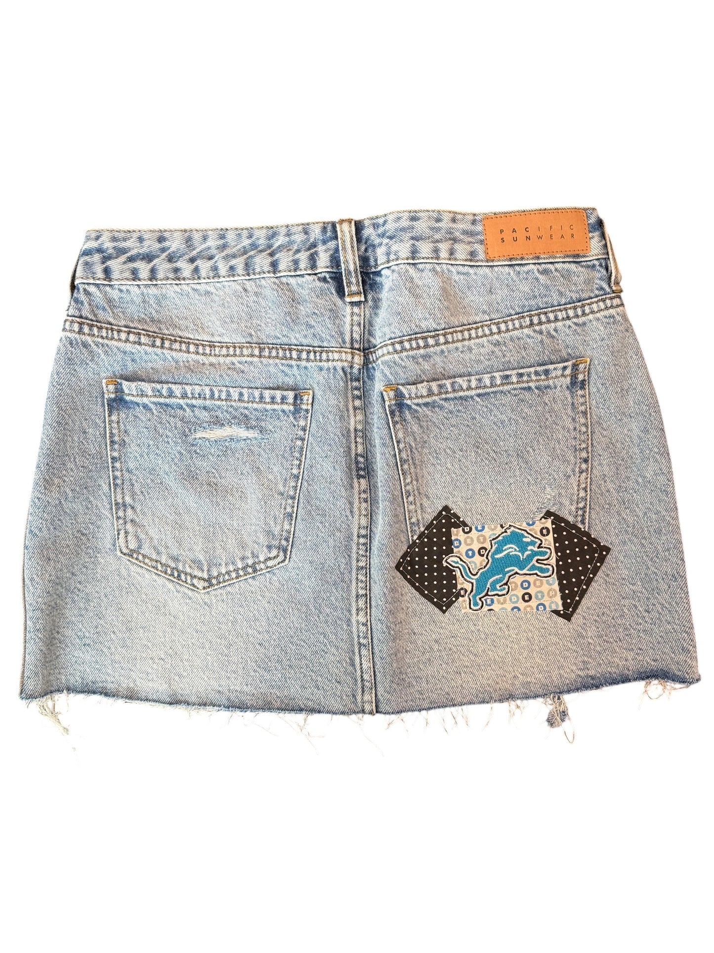 Light wash denim mini skirt shown from the back, featuring a distressed frayed hem, two back pockets, and a Detroit Lions patch on the right pocket.