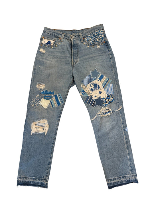 Light blue denim jeans with distressed rips and colorful patchwork appliques in blue, white, and yellow, laid flat on a white background.