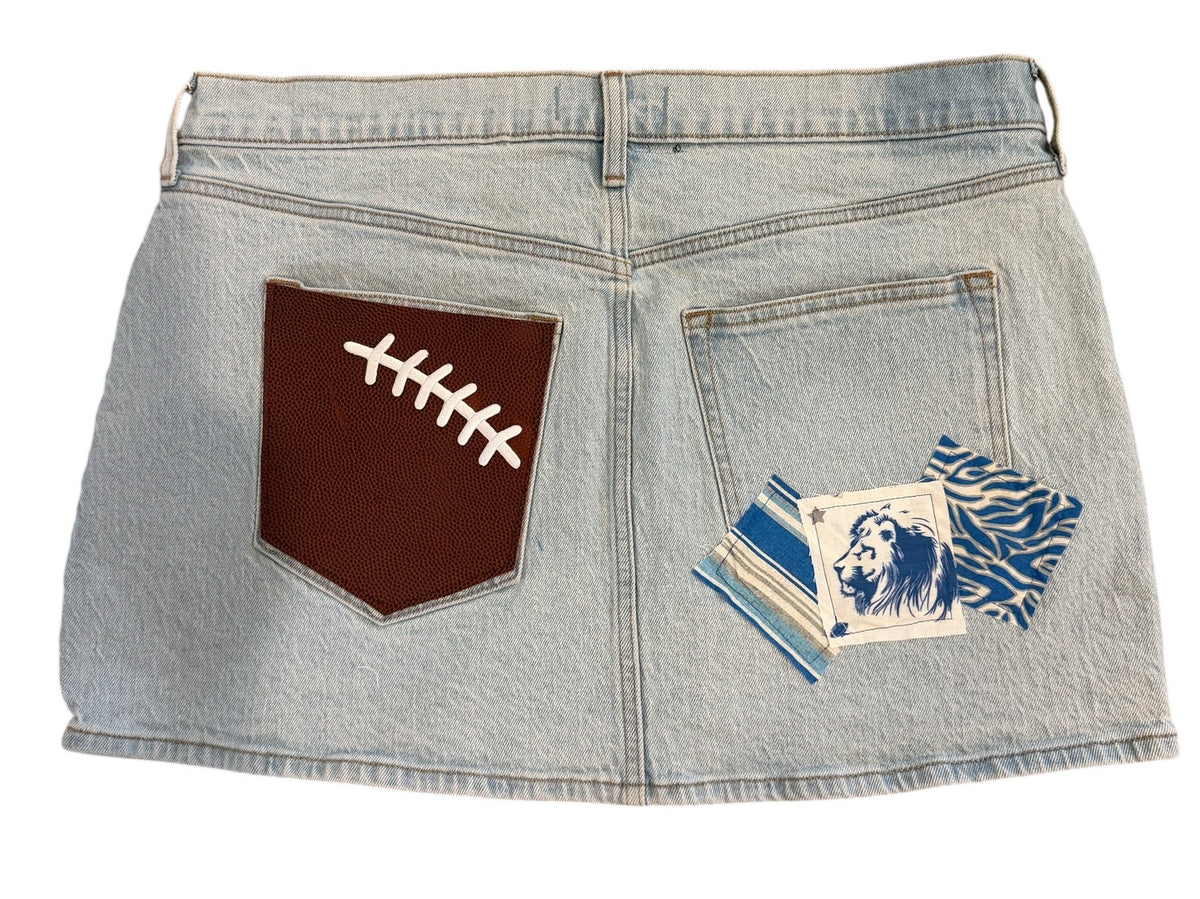 Light wash denim shorts with a brown faux-leather football patch on the back pocket and a blue-and-white tiger patch on the front pocket, shown on a white background.