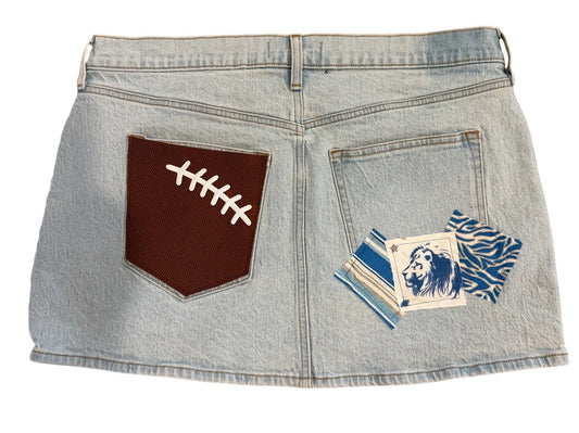 Light wash denim shorts with a brown faux-leather football patch on the back pocket and a blue-and-white tiger patch on the front pocket, shown on a white background.