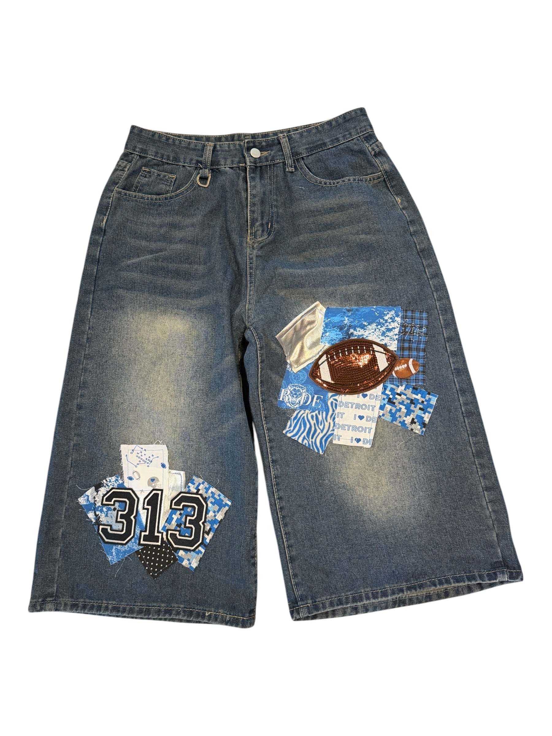 A pair of blue denim shorts with distressed fading and custom patchwork appliques on the thighs. The patches feature blue and white patterns, a black and white '313' design, and a brown football patch.