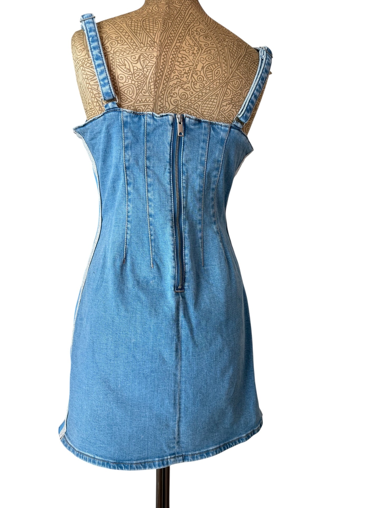 A light blue denim mini dress with a zip-up back, displayed on a tan patterned dress form against a white background.