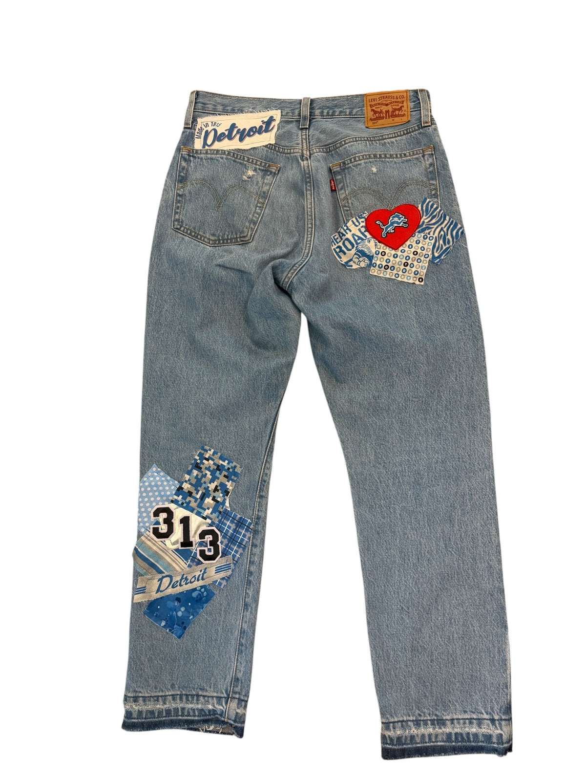 Light blue denim jeans with decorative patchwork back pockets featuring blue, red, and white designs, laid flat on a white background.