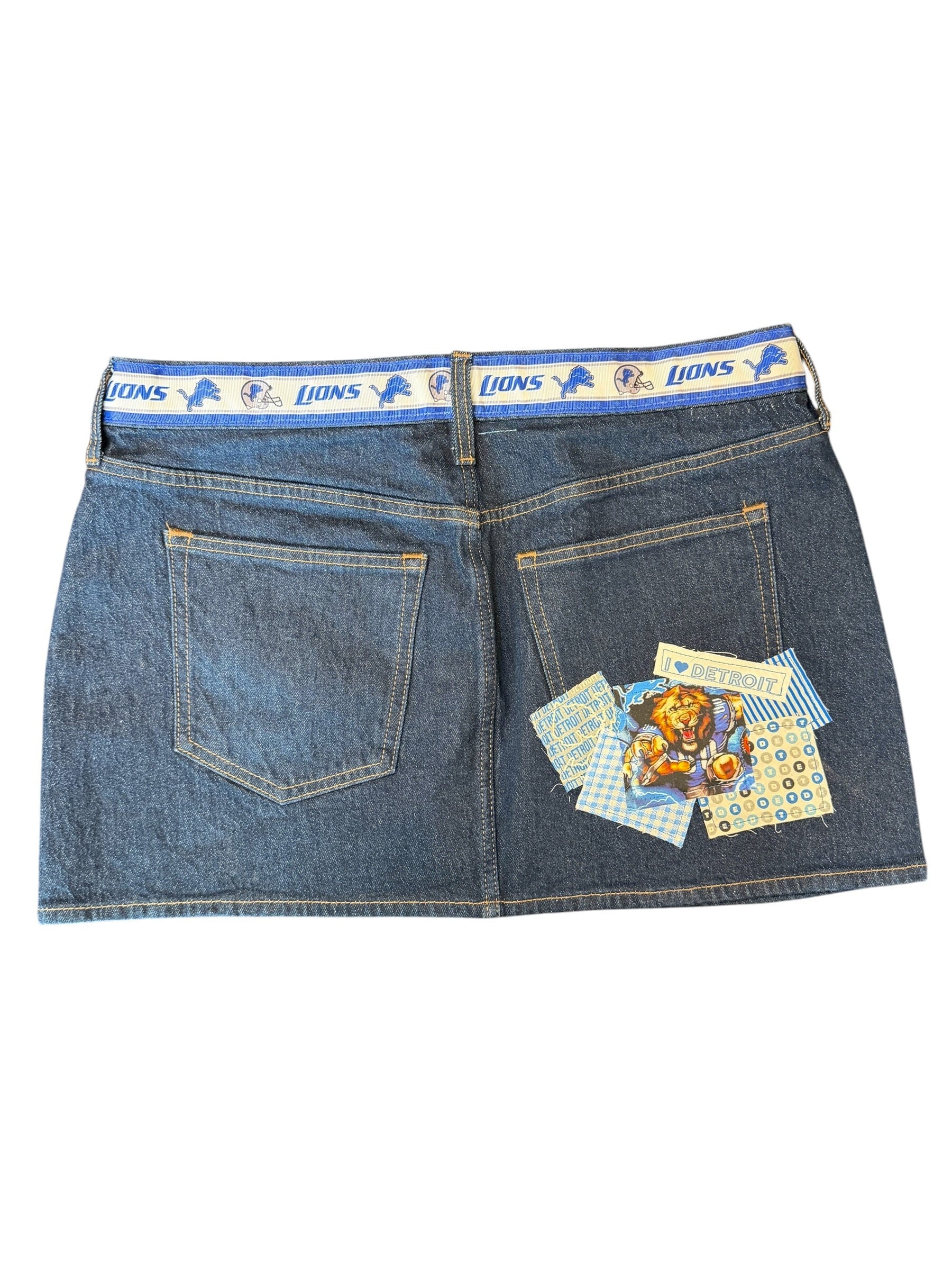 A pair of folded blue denim shorts with decorative printed patches on the back pockets and a blue waistband featuring the Lions logo, shown against a plain white background.