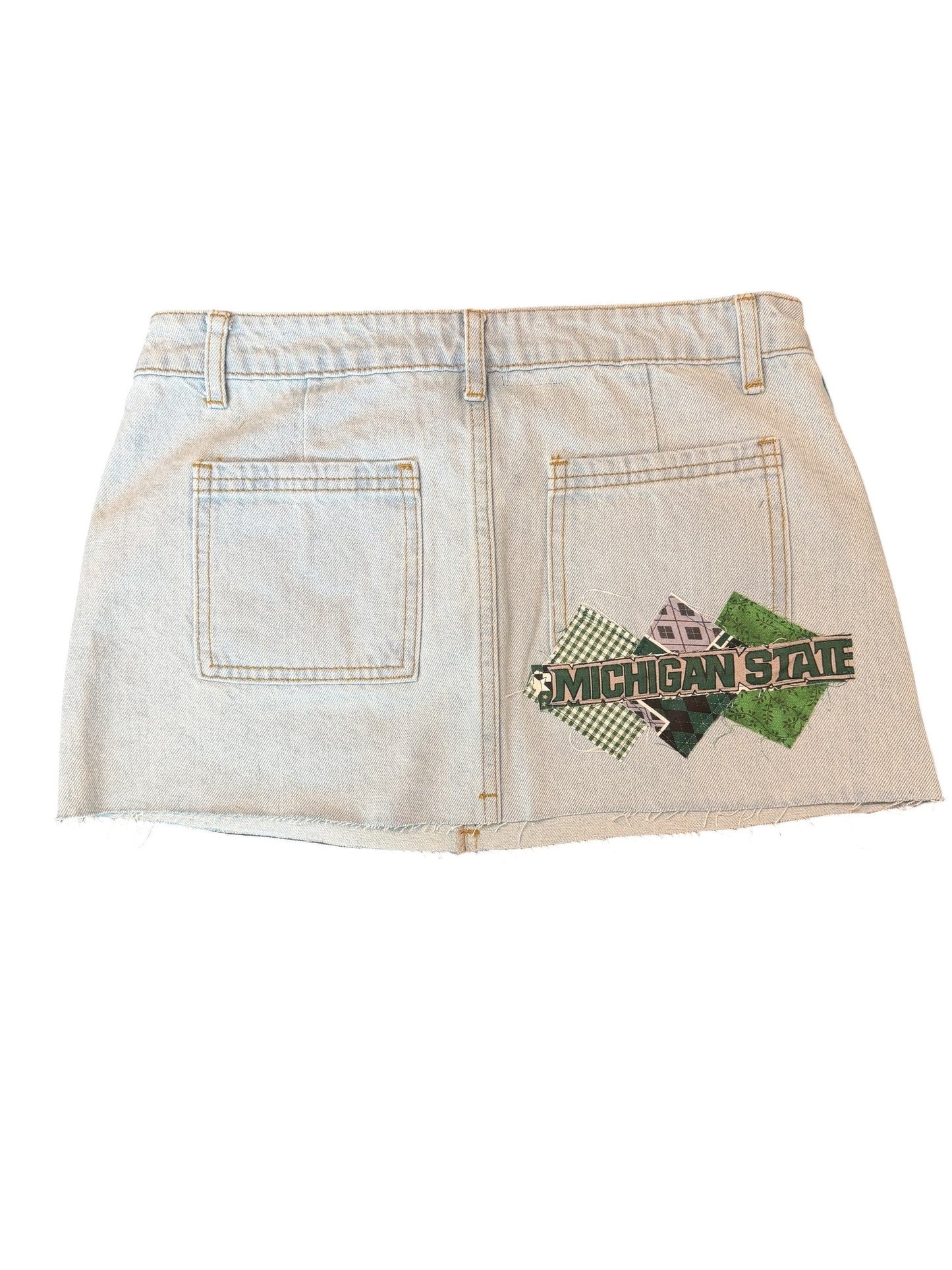 A light-wash denim mini skirt with a distressed, faded finish and a Michigan State Spartans logo patch on the back right pocket area, shown against a plain white background.