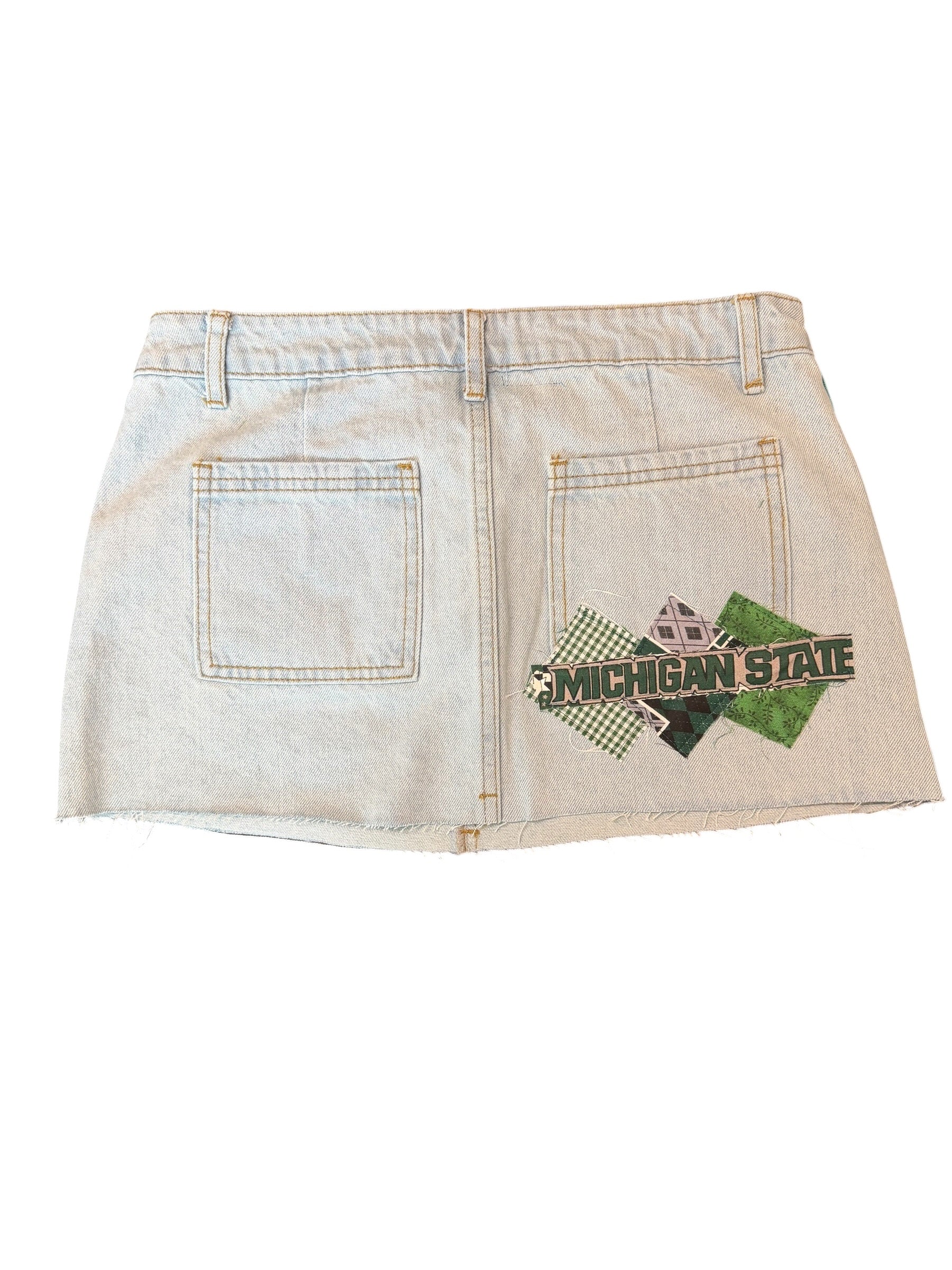A light-wash denim mini skirt with a distressed, faded finish and a Michigan State Spartans logo patch on the back right pocket area, shown against a plain white background.