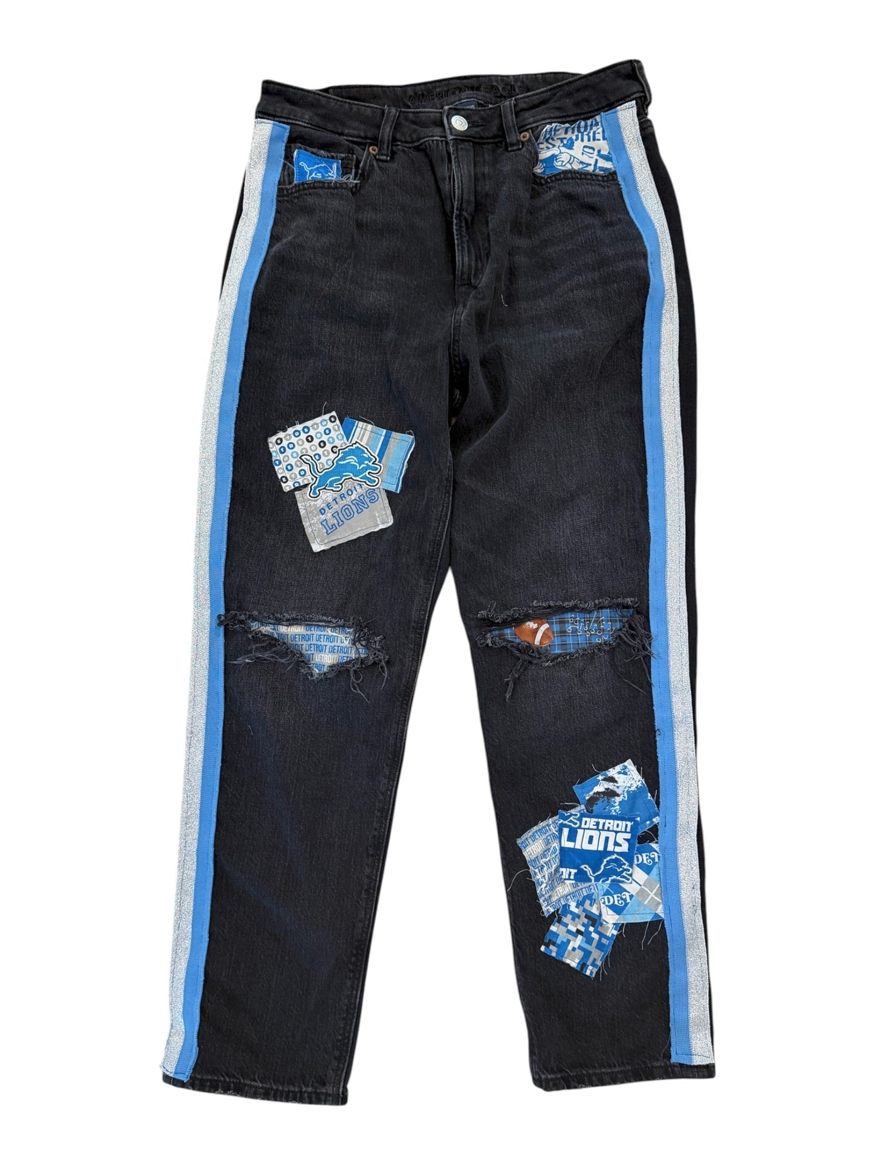 A pair of black distressed jeans with ripped details, blue and white graphic patches, and a light blue and white stripe down the outer side of each leg, shown on a plain white background.