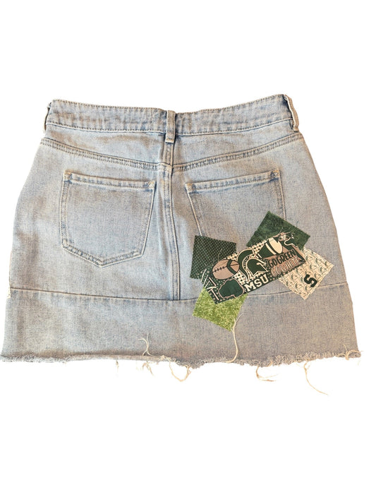 Light-wash denim shorts with a raw, frayed hem and decorative vintage-style fabric patches sewn onto the back pocket area, shown flat on a white background.