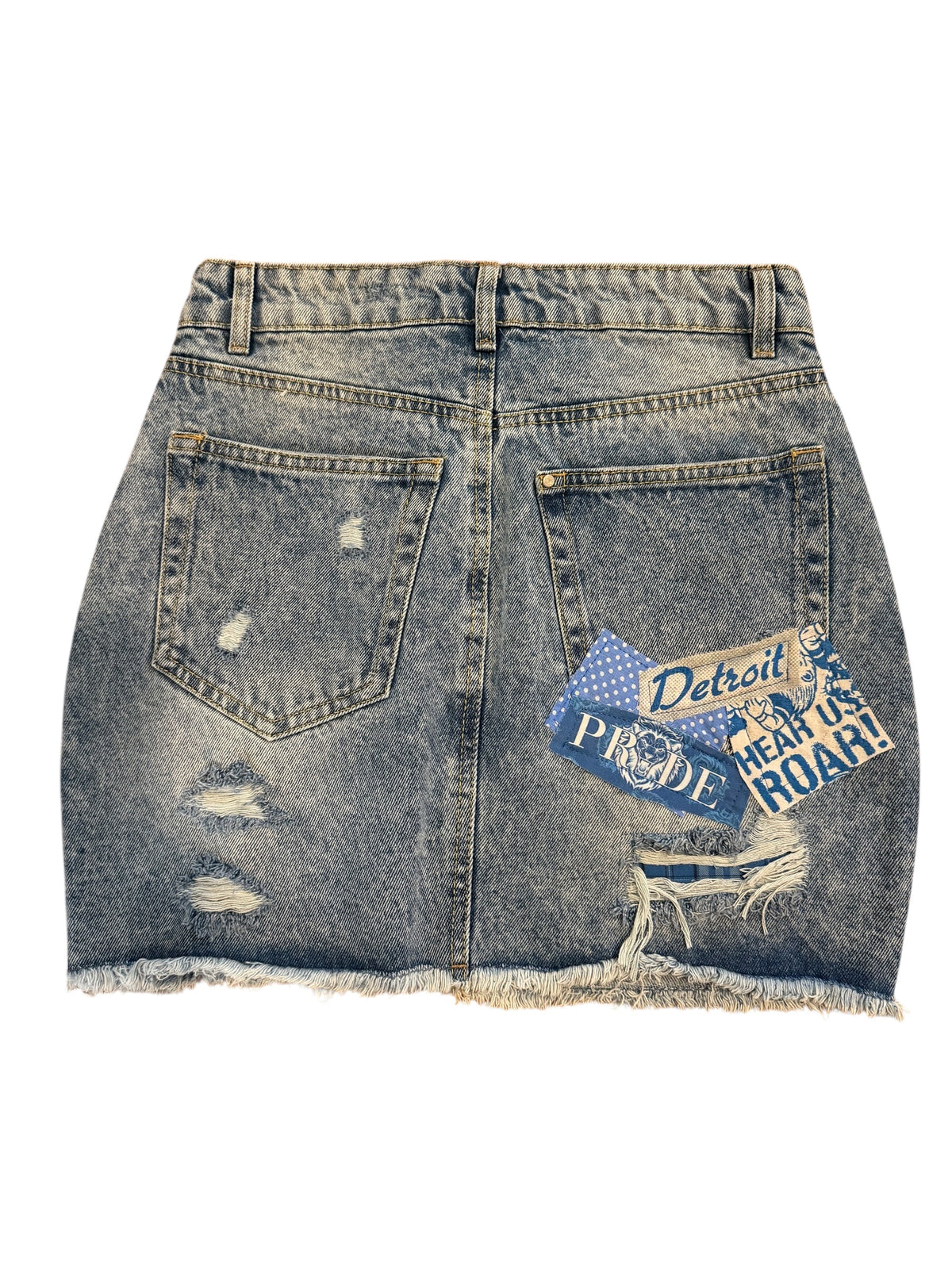 A distressed denim mini skirt with a frayed hem, featuring a blue and white 'Detroit Proud Teen Us Roar!' patch on the back right pocket, shown against a plain white background.
