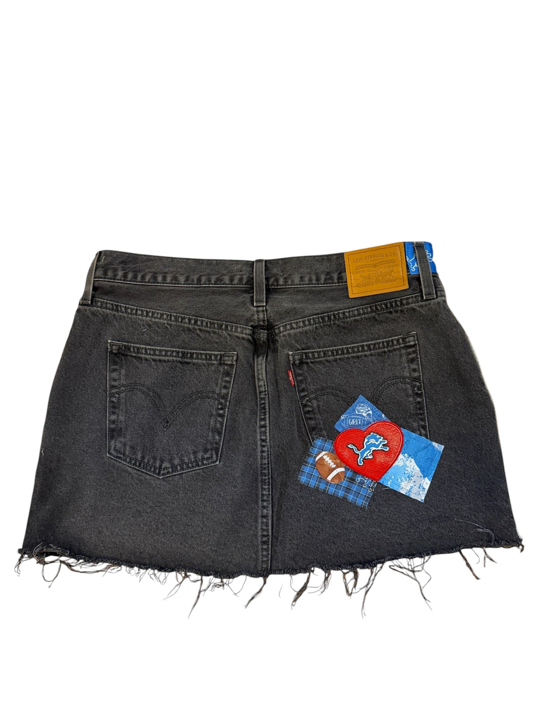 A pair of dark gray denim shorts with raw, frayed edges, featuring a colorful patchwork quilted design on the back pocket and a yellow leather patch on the left side, shown against a plain white background.