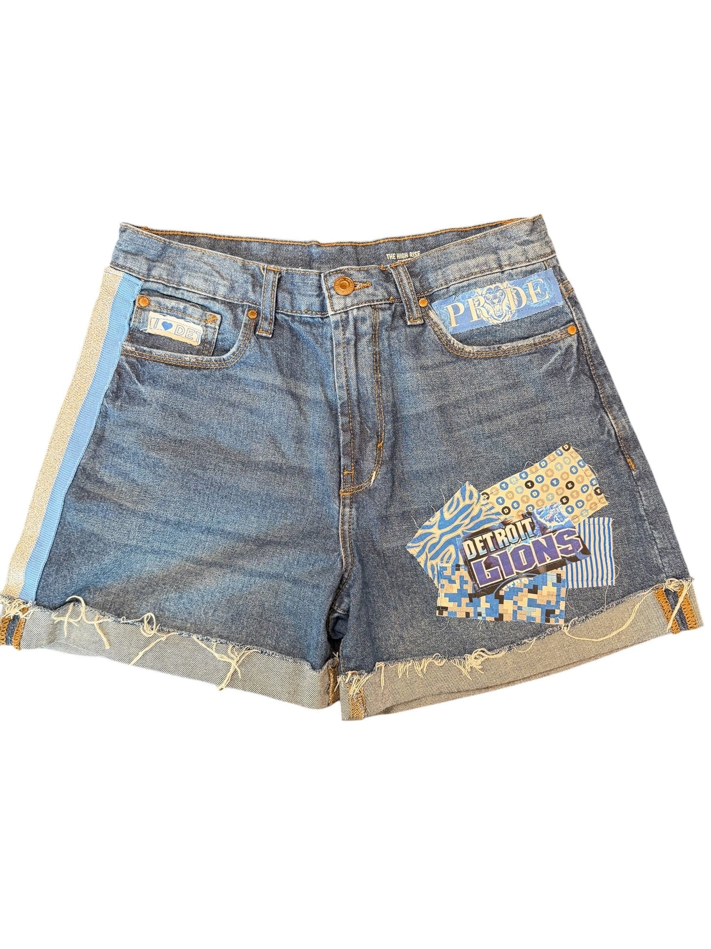 A pair of distressed denim shorts made from repurposed jeans, featuring colorful patchwork fabric patches on the front and raw, frayed edges. The shorts are shown flat against a solid white background.