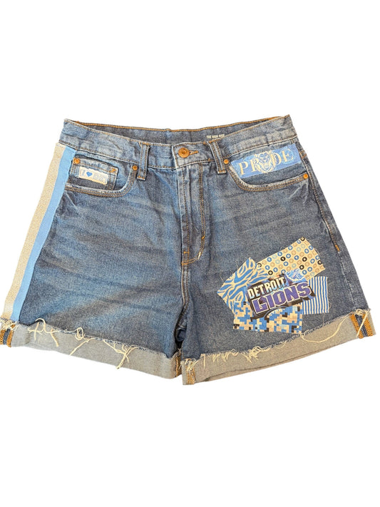 A pair of distressed denim shorts made from repurposed jeans, featuring colorful patchwork fabric patches on the front and raw, frayed edges. The shorts are shown flat against a solid white background.