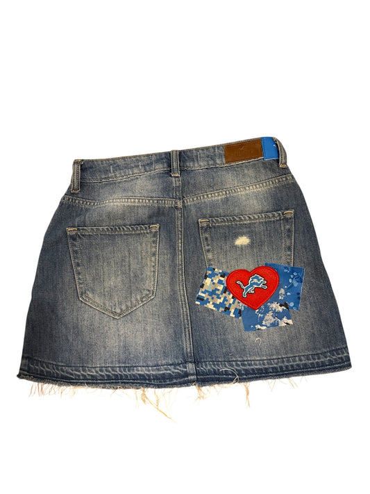 A denim skirt with a raw, frayed hem and distressed details, featuring a colorful patch on the back pocket with a red heart and blue patterned fabric.