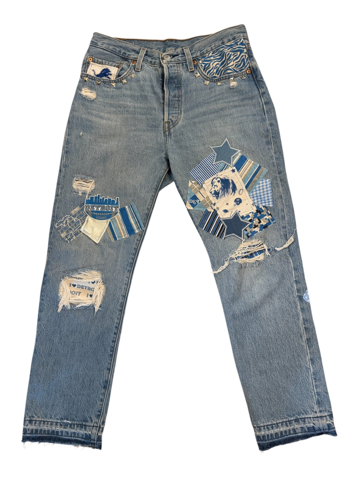 Light blue denim jeans with extensive distressed rips and colorful patchwork appliques in blue, beige, and white, laid flat on a white background.