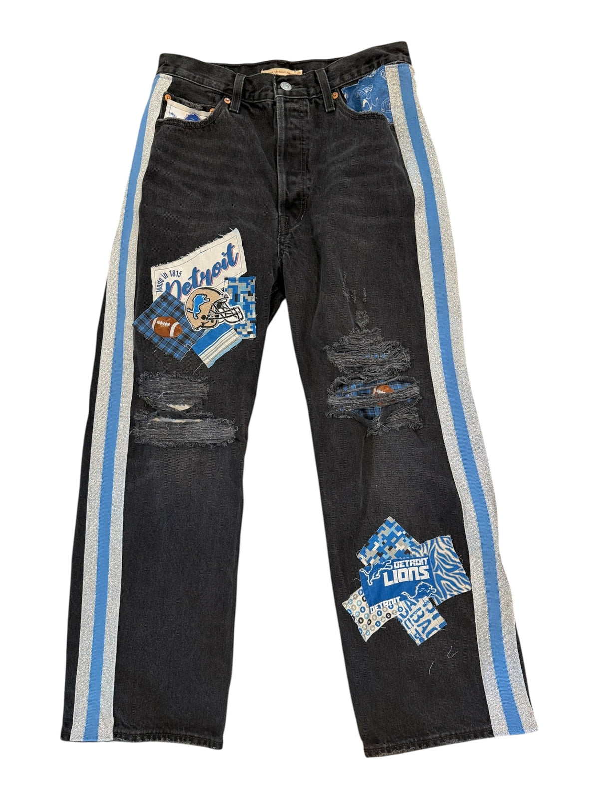 A pair of heavily distressed black denim jeans laid flat on a white background, featuring light blue and gray side stripes, ripped details, and multiple colorful graphic patches.