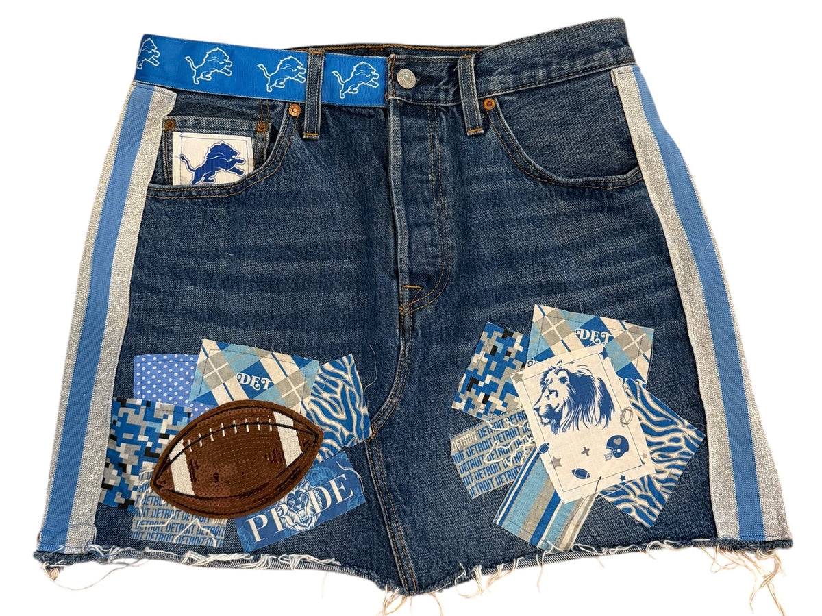 A pair of blue denim shorts featuring a patchwork design with various sports-themed prints, including a football patch, a blue and white patterned patch, and a small white patch with a blue logo. The shorts are laid flat on a white background.