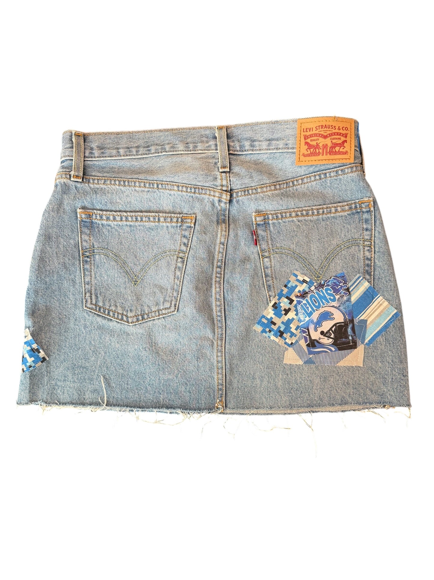 Light wash denim mini skirt shown from the back, featuring two back pockets, a classic orange Levi's waist patch, and decorative blue and white patterned fabric patches on the back pockets and left side seam.