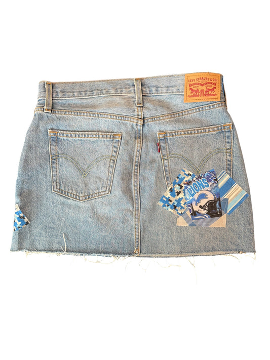 Light wash denim mini skirt shown from the back, featuring two back pockets, a classic orange Levi's waist patch, and decorative blue and white patterned fabric patches on the back pockets and left side seam.