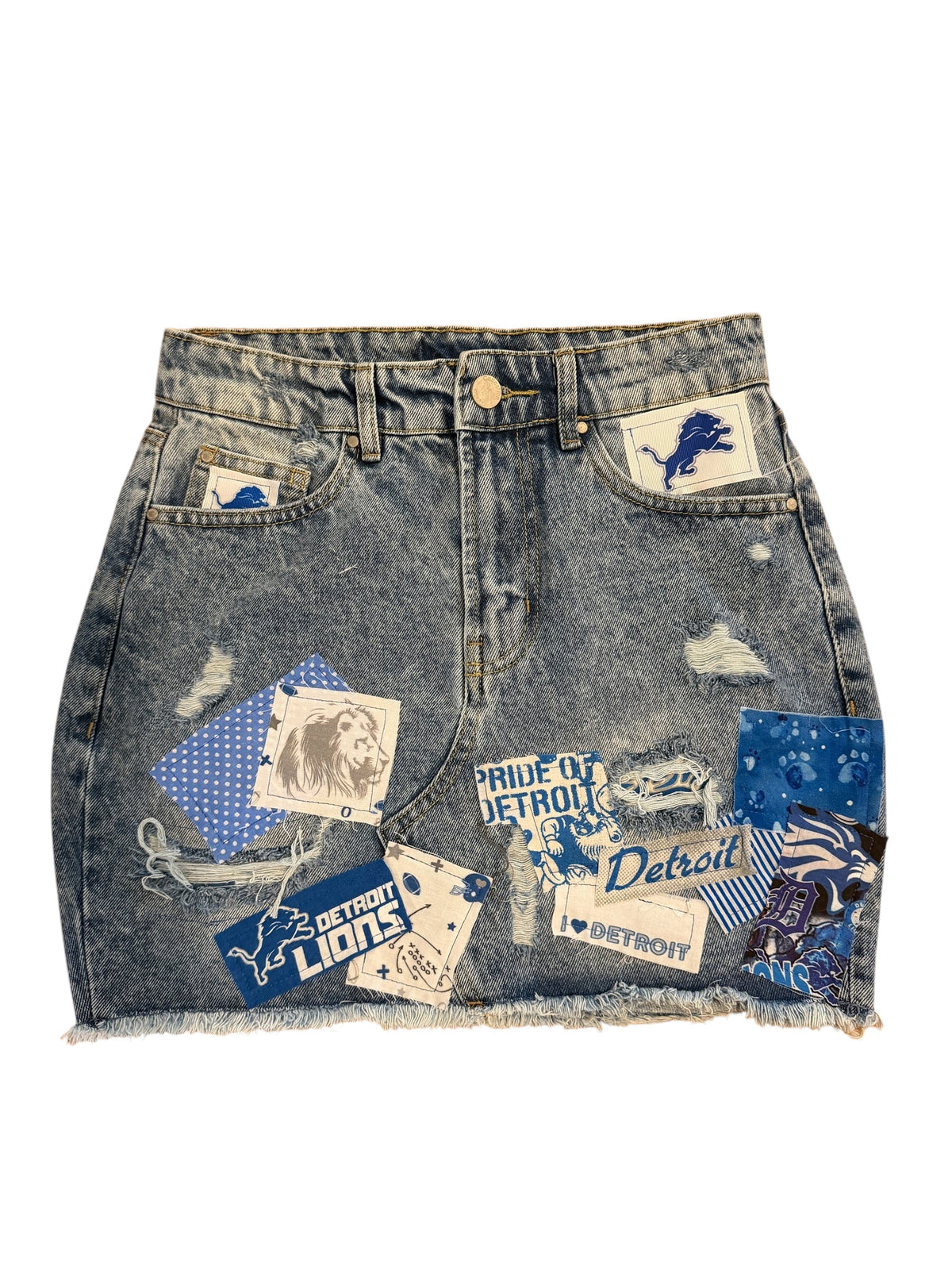A distressed denim mini skirt with a raw frayed hem, featuring various Detroit-themed patches and stickers on the front pockets and sides.