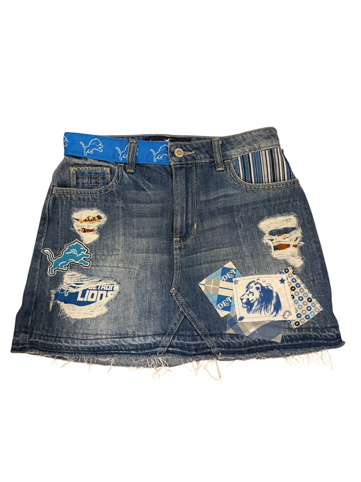 A pair of heavily distressed blue denim shorts featuring ripped details, frayed edges, and multiple colorful patches and appliques, including a blue horse patch and a striped pocket detail, shown on a plain white background.