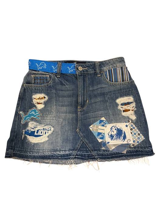 A pair of heavily distressed blue denim shorts featuring ripped details, frayed edges, and multiple colorful patches and appliques, including a blue horse patch and a striped pocket detail, shown on a plain white background.