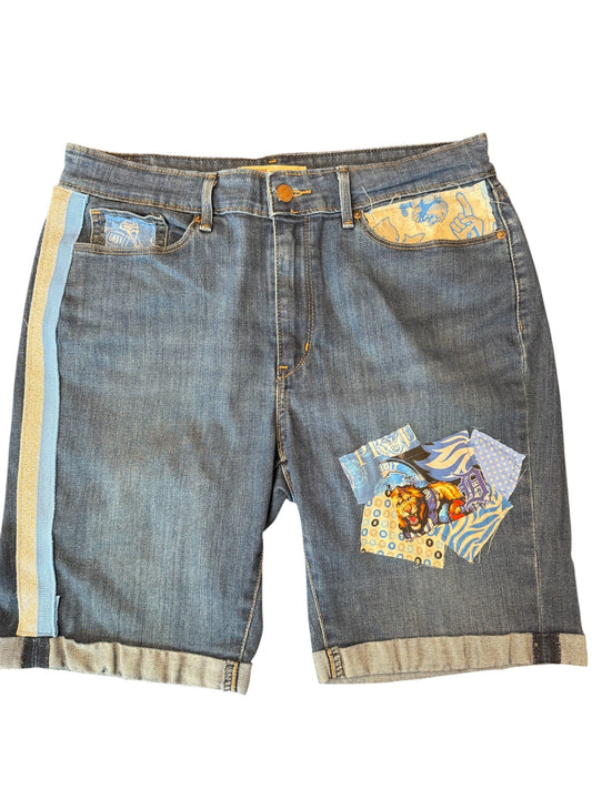 A pair of blue denim shorts featuring decorative patchwork fabric panels on the back pockets and rolled cuffs, displayed flat against a white background.
