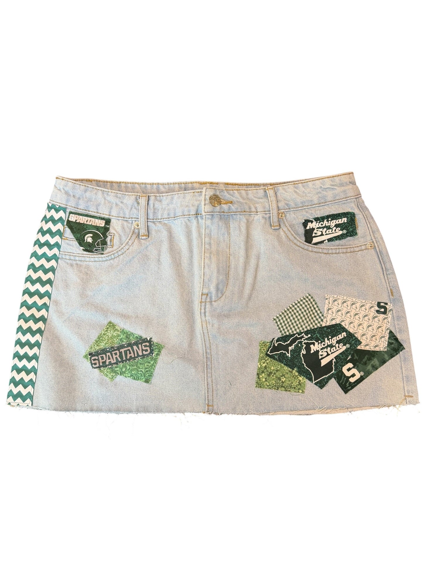 A pair of light-wash denim shorts featuring green and white chevron trim along the waistband and multiple green graphic patches with text and patterns on the front, displayed flat against a white background.