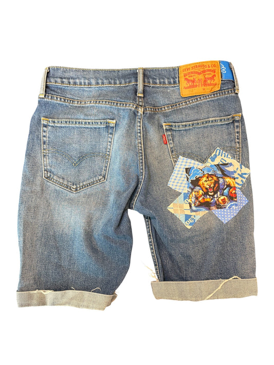Back view of light blue denim shorts with rolled cuffs, featuring a colorful patchwork graphic on the right back pocket and a yellow Levi's waistband label.