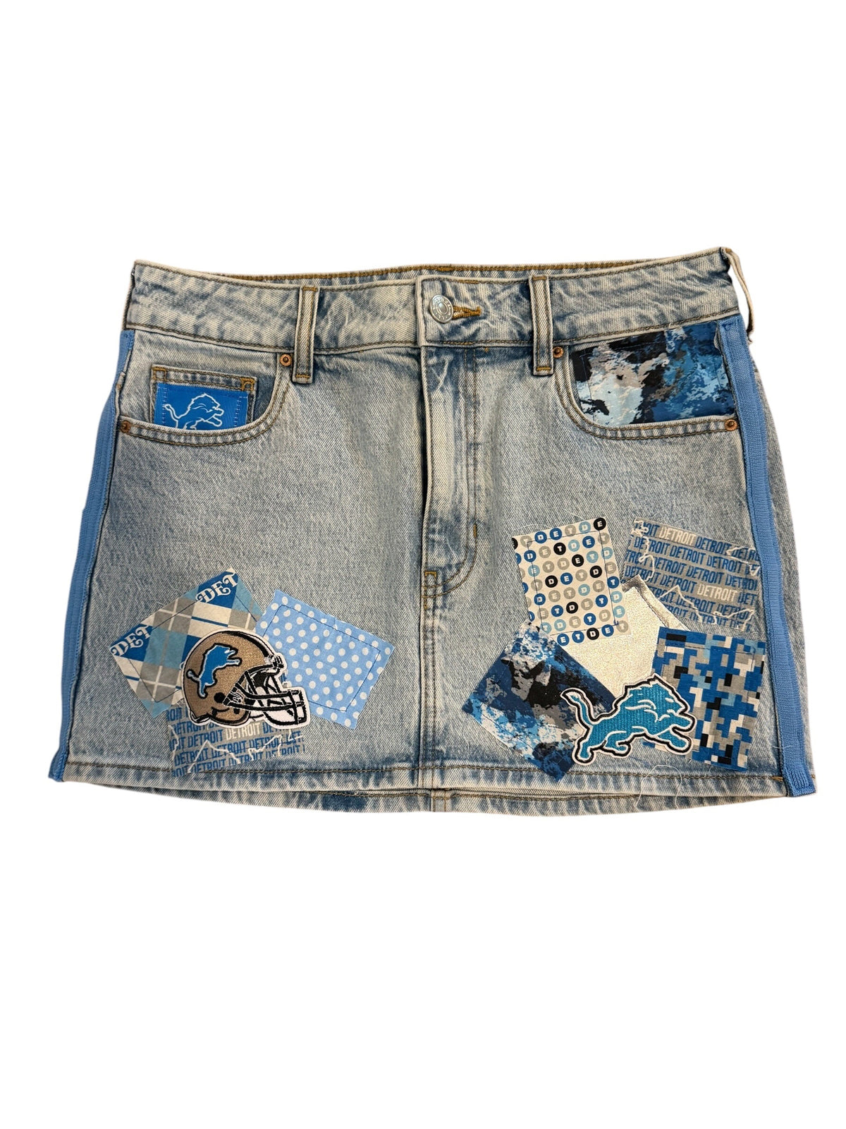 Light-wash denim shorts with a patchwork collage design featuring blue, white, and black patterned fabric panels and graphic patches on the back pockets, shown against a plain white background.