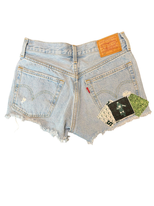 Light wash blue denim shorts with a raw frayed hem, featuring a prominent orange Levi's back patch and a small red tab on the right side, shown against a plain white background.