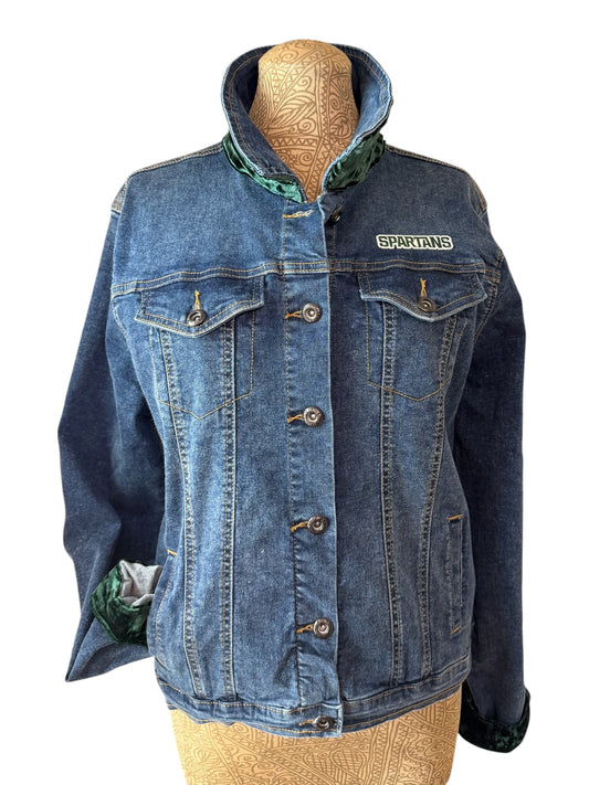 A blue denim jacket with a high collar and a 'SPARTANS' patch on the chest, displayed on a tan mannequin torso against a white background.
