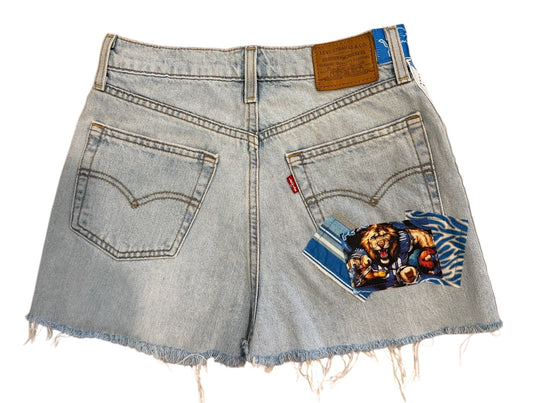 Light-wash denim shorts with a distressed, frayed hem and a colorful graphic patch on the back pocket, shown flat on a white background.