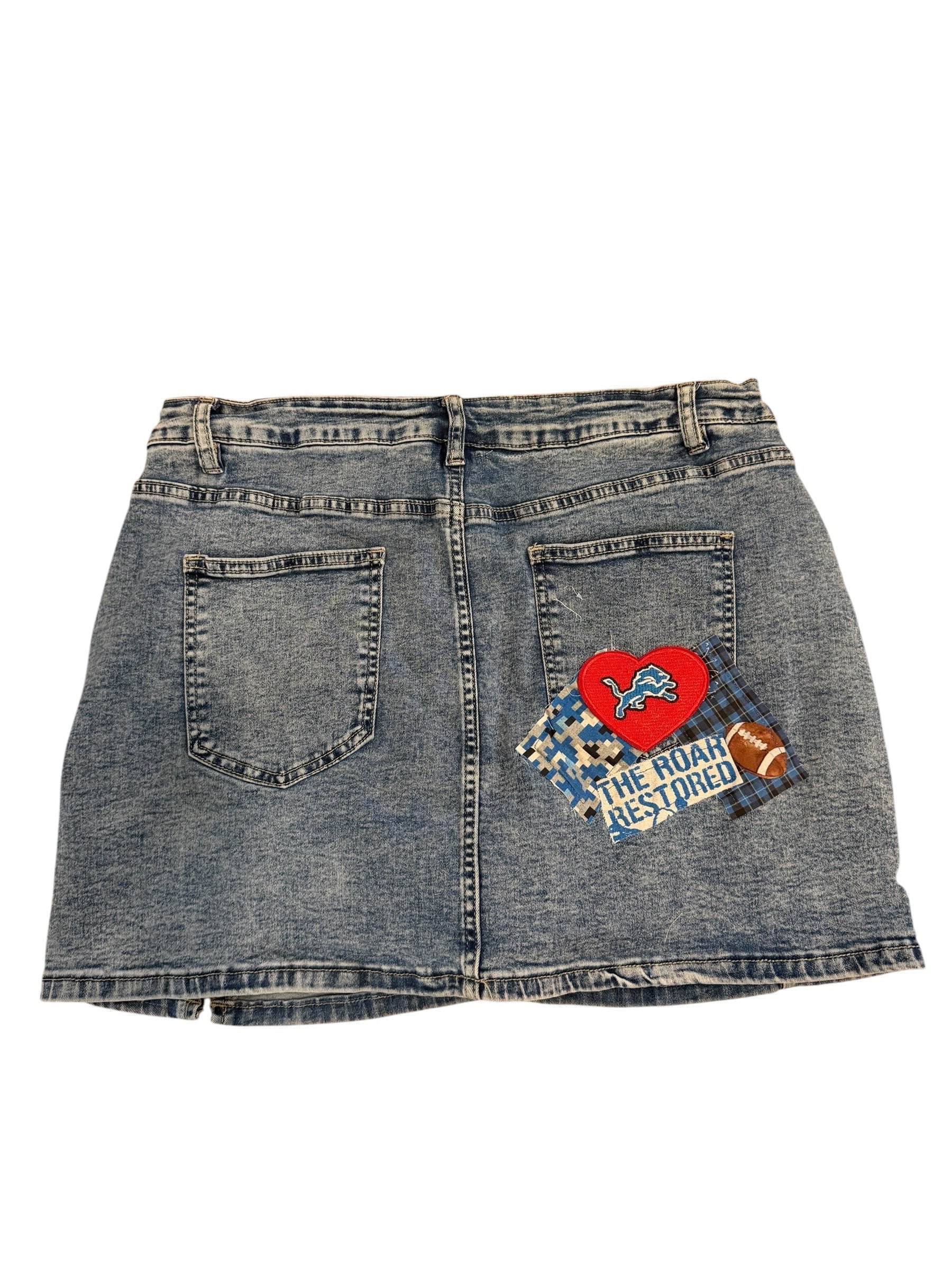 A pair of faded blue denim shorts shown from the back, featuring a red heart patch and a blue patterned patch with the text 'THE ROCK IS YOUNG' on the left side.