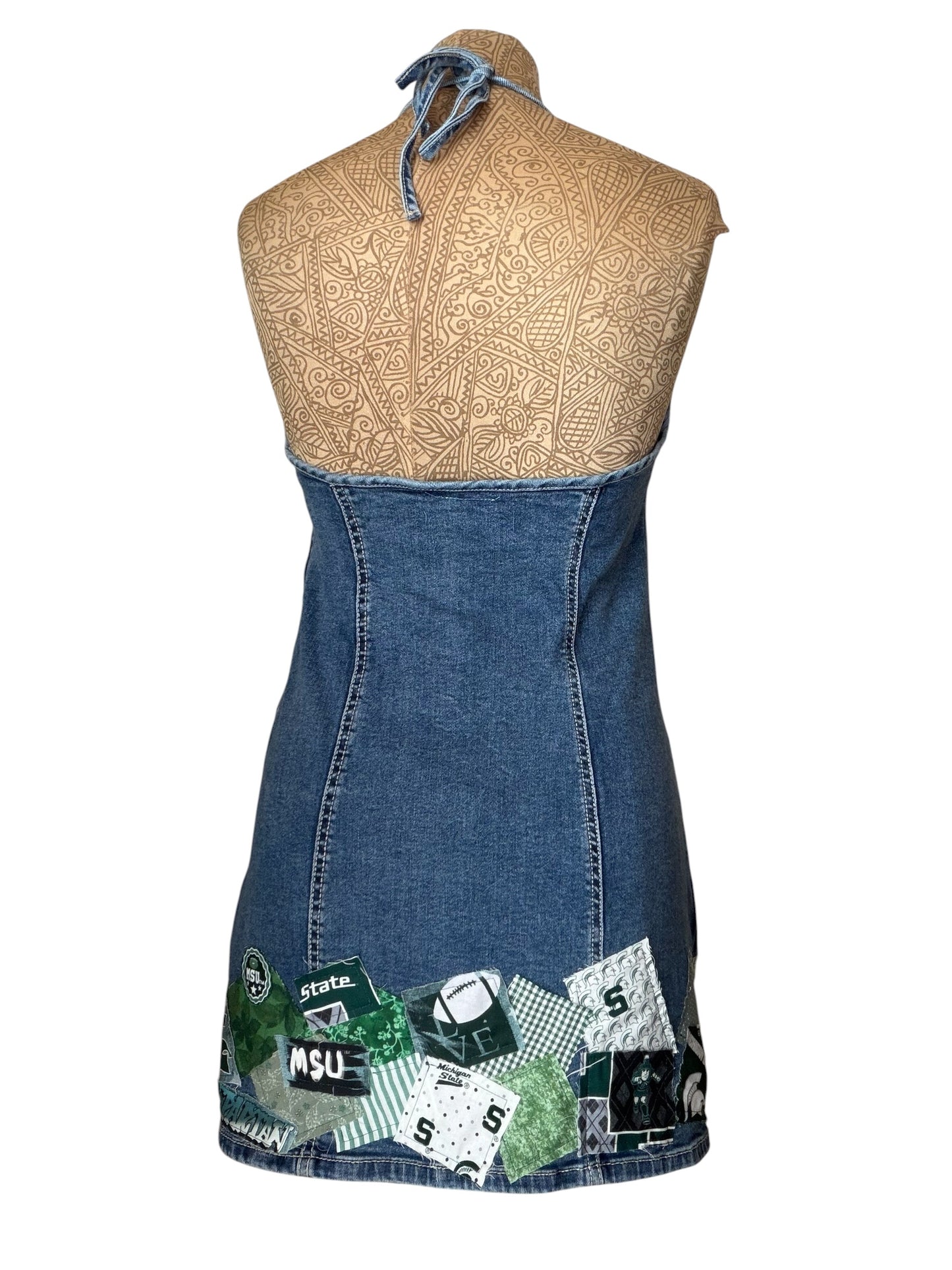 A sleeveless halter-neck dress displayed on a beige mannequin torso against a white background. The dress has a textured beige upper section and a blue denim lower section with a green and white patchwork collage at the hem.