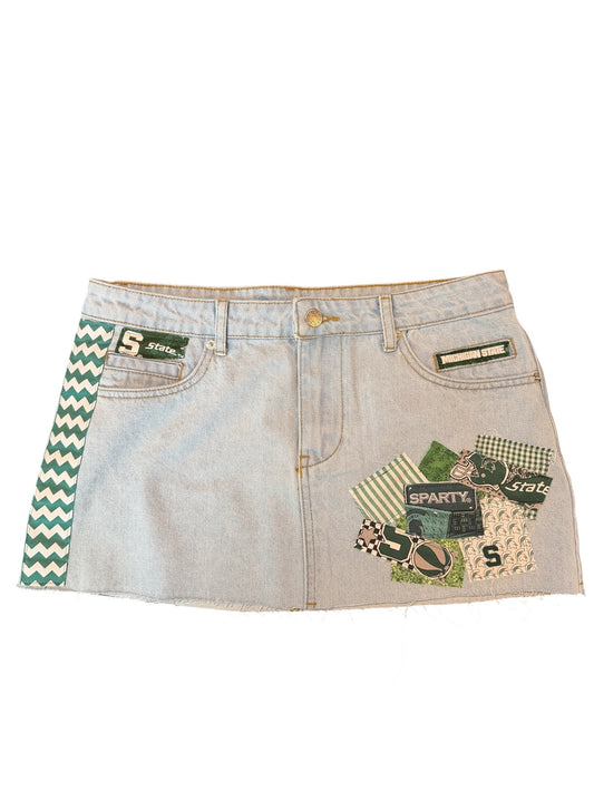 A pair of light-wash denim shorts featuring green and white chevron patterned trim along the back waistband and a green graphic patch with the number 5 on the front pocket.