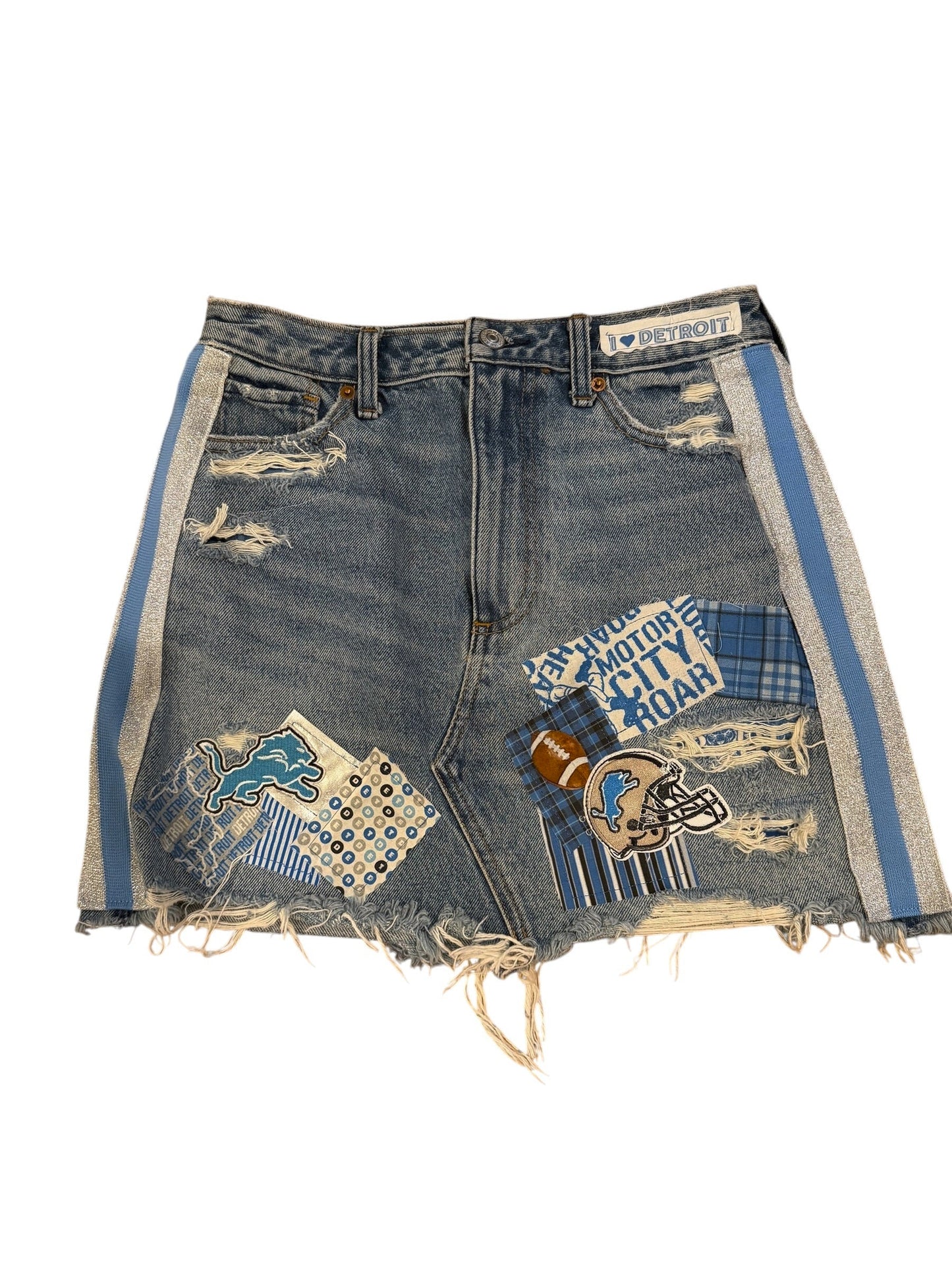 Distressed denim shorts with frayed edges, featuring blue and white plaid patches, a football patch, and a blue and white striped trim, shown on a white background.