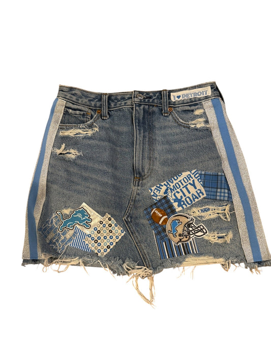Distressed denim shorts with frayed edges, featuring blue and white plaid patches, a football patch, and a blue and white striped trim, shown on a white background.