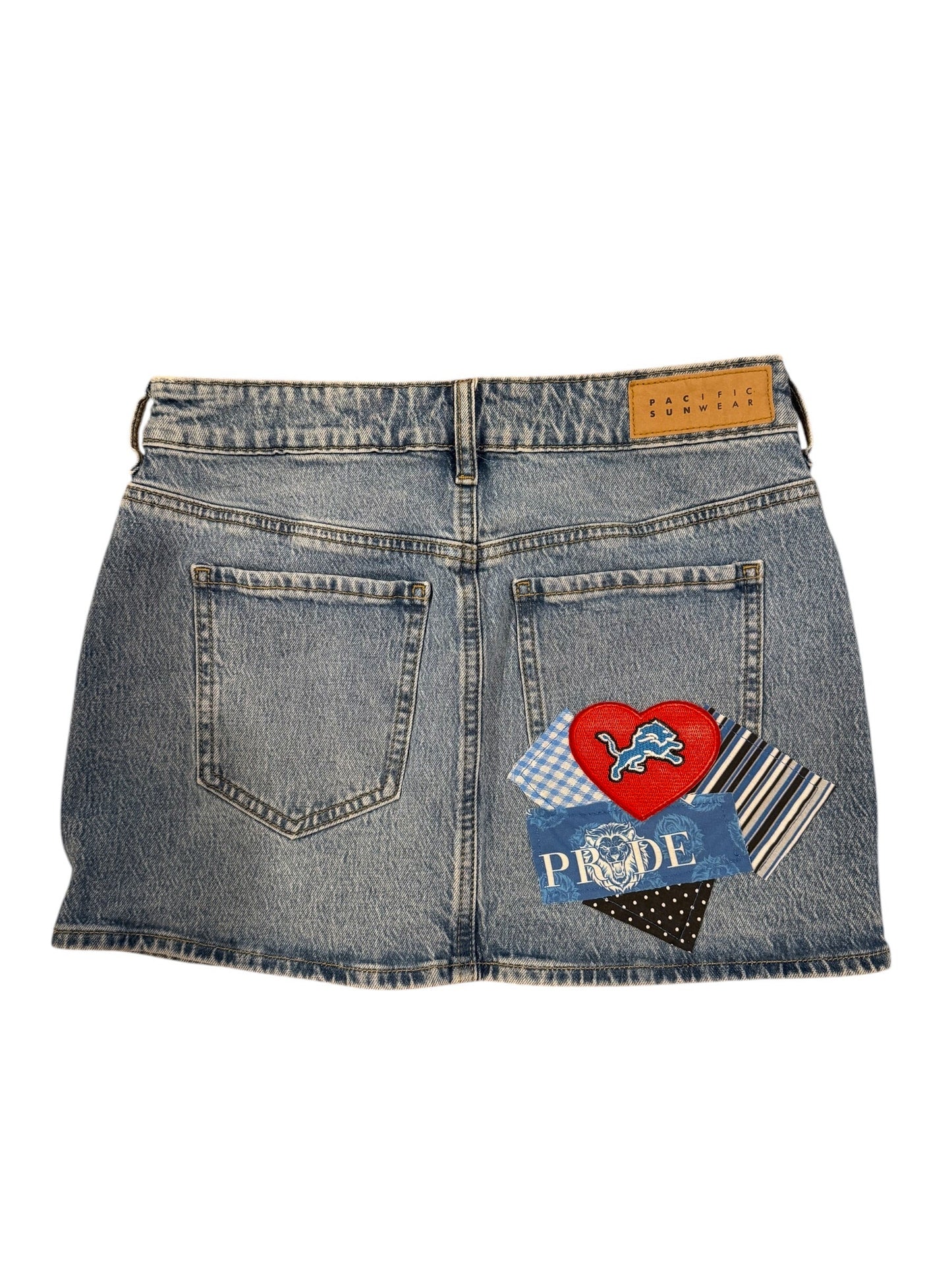 A pair of light blue denim jeans laid flat on a white background, decorated with colorful patches on the back pocket area. The patches include a red heart with a horse, a blue checkered square, a black and white polka dot triangle, and striped fabric.