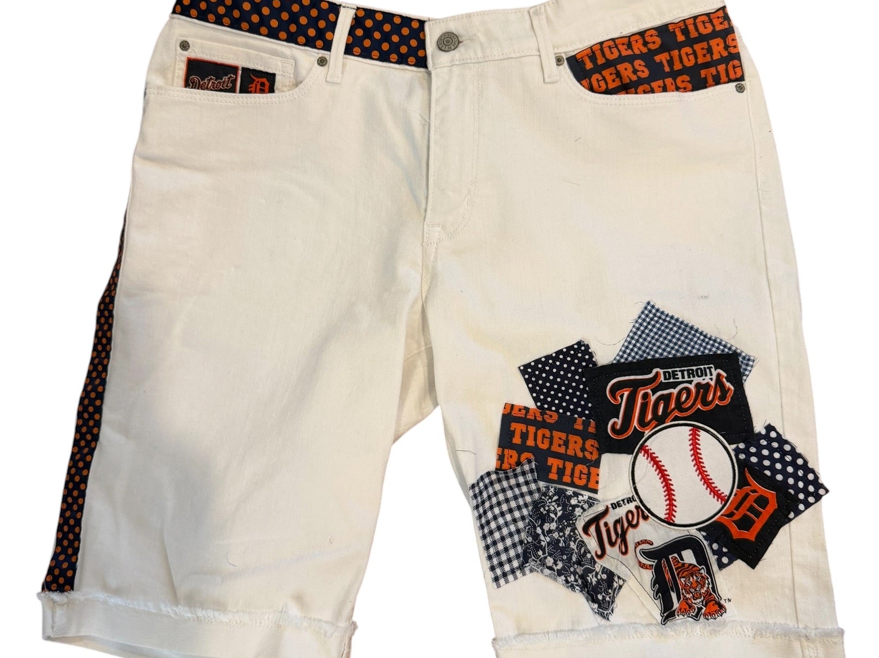 A pair of off-white denim shorts featuring a Texas Rangers baseball-themed patchwork graphic on the right leg and a patterned orange-and-black waistband, displayed against a plain white background.