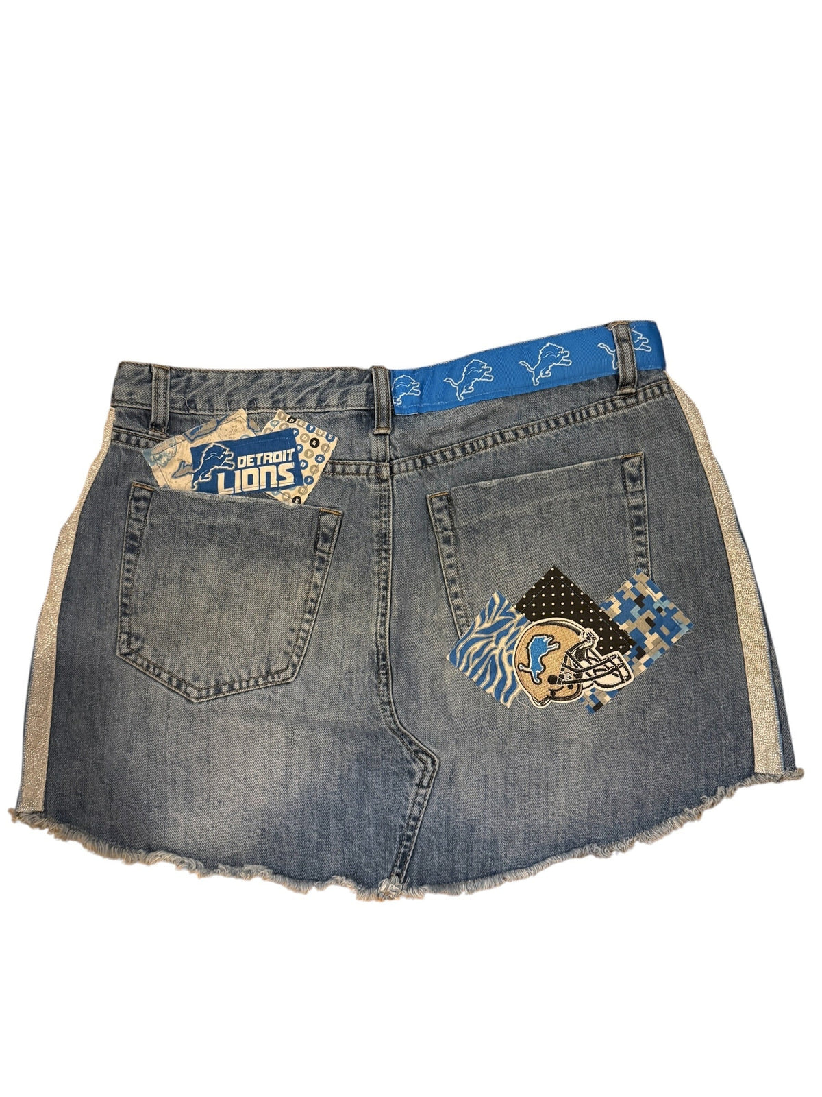 A pair of distressed denim shorts with frayed edges, featuring two decorative embroidered patches on the back pockets and a blue patterned waistband.
